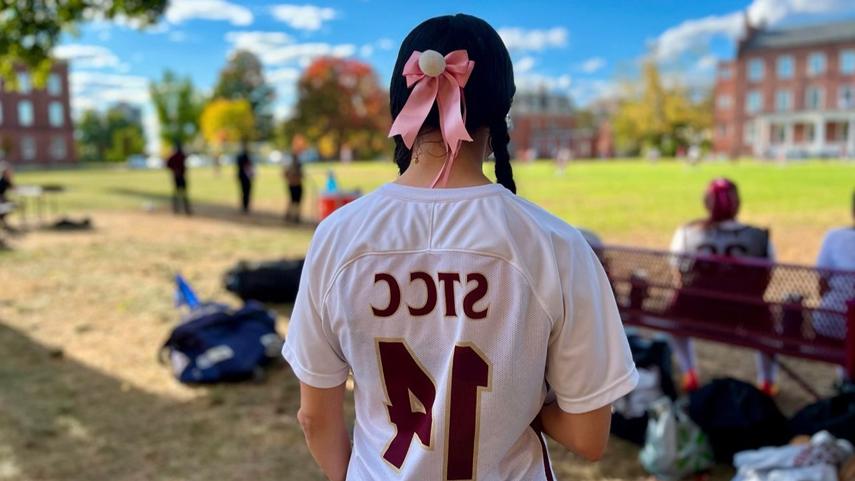 women's soccer player looking off at game with pink ribbbon in her hair in braids